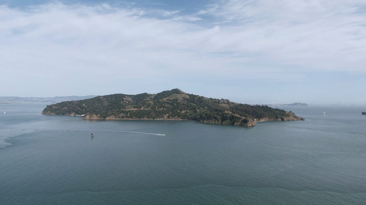 A wooded island in calm bay water under a pale sky, with a boat passing
