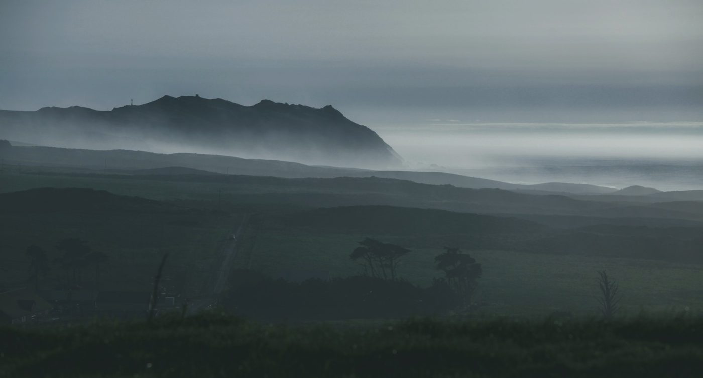 Mist drifting over dark hills below a headland