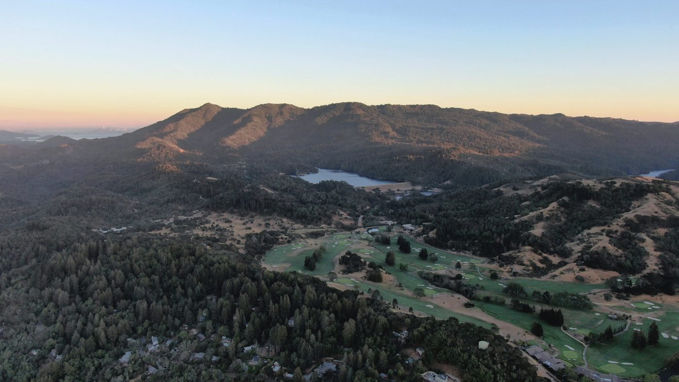 Mount Tamalpais in low golden light, above forested hills, a small lake and a golf course